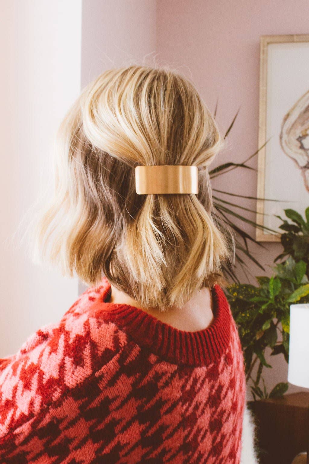 Person with a gold hair clip in their blonde hair, wearing a red sweater indoors.