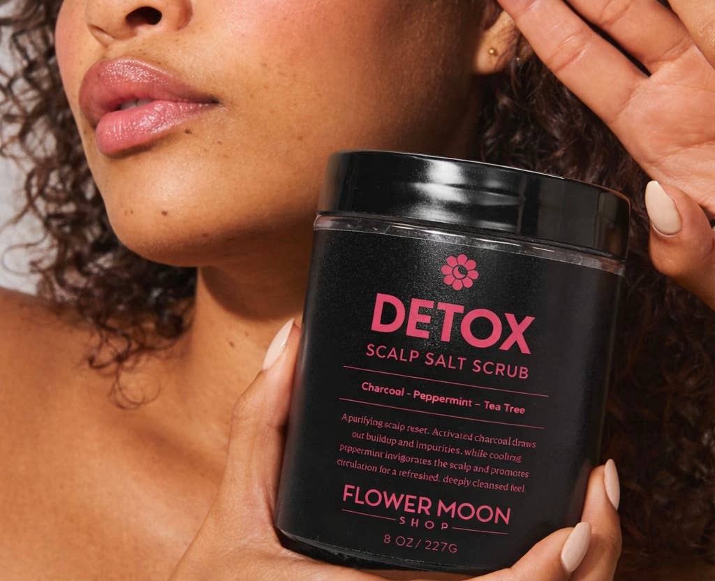 Person holding a jar of 'Detox Scalp Salt Scrub' by Flower Moon Shop.