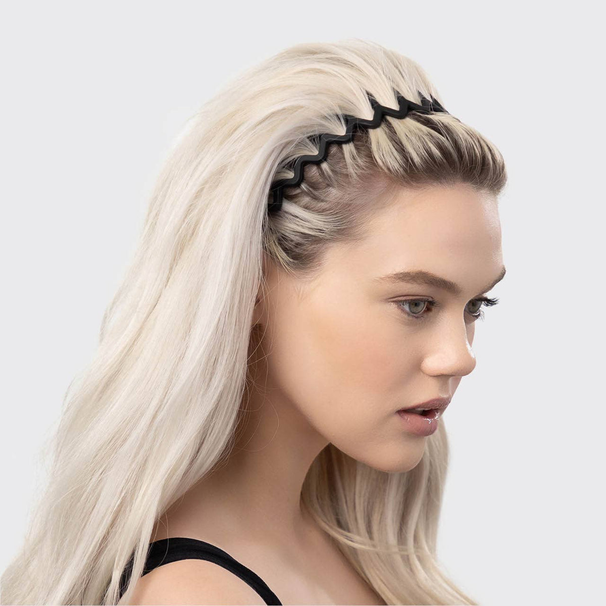 Woman with long blonde hair slicked back with a black zig zag headband