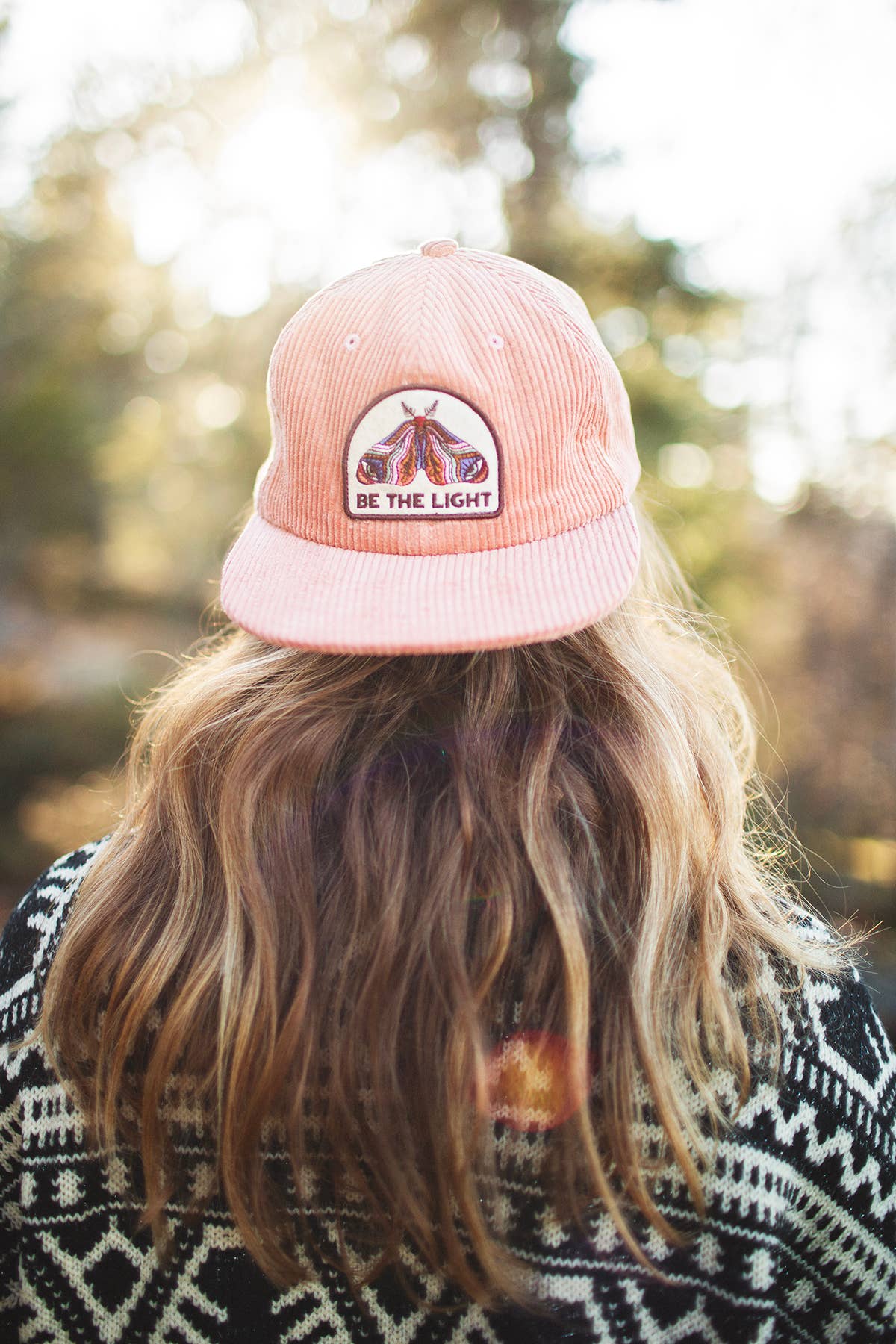 Woman with long wavy blonde hair seen from behind wearing the salmon pink Be The Light corduroy snapback