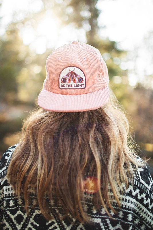 Woman with long wavy blonde hair seen from behind wearing the salmon pink Be The Light corduroy snapback
