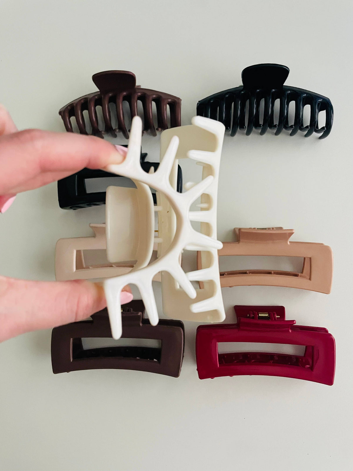 Hand holding a white silicone bendable rectangle claw clip open above the brown and red colorways