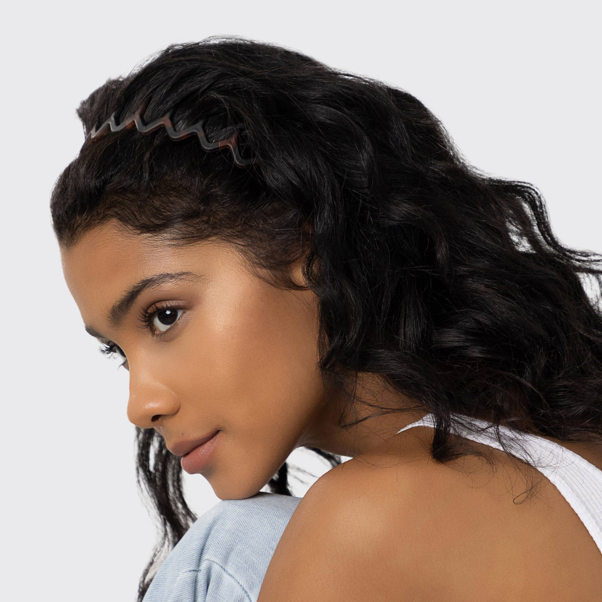 Woman with long dark curly hair wearing a black zig zag headband