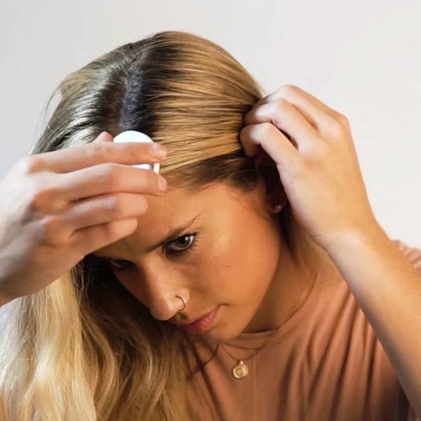 Woman with blonde hair applying root touch-up powder at her part