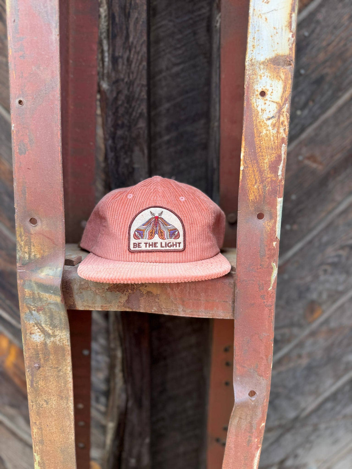 Be The Light corduroy cap sitting on a weathered wooden ladder against a barn door