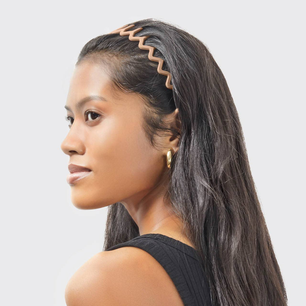 Side view of a tan zig zag headband holding long dark hair back off the face